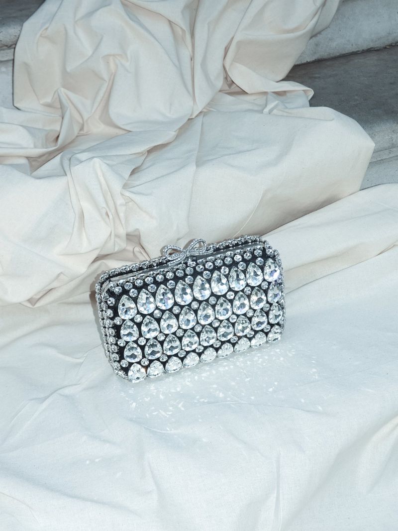 Elegant black and silver clutch purse adorned with crystals, lying on a white cloth in a studio setting, catching the light.