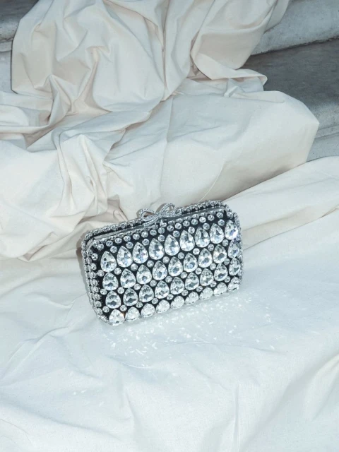 Elegant black and silver clutch purse adorned with crystals, lying on a white cloth in a studio setting, catching the light.