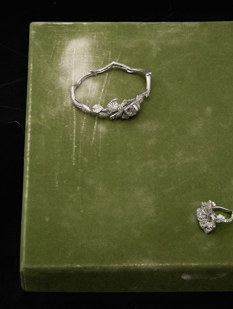 Close-up of silver floral jewelry set on a green box against a dark background, showcasing intricate designs and fine craftsmanship.
