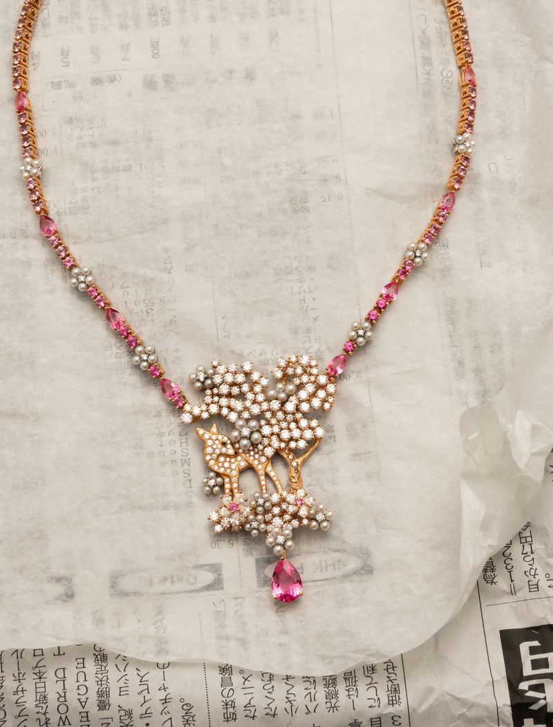 Close-up of a necklace with pink and white gemstones, featuring a deer and tree design, on a newspaper-printed surface. Jewelry photography.
