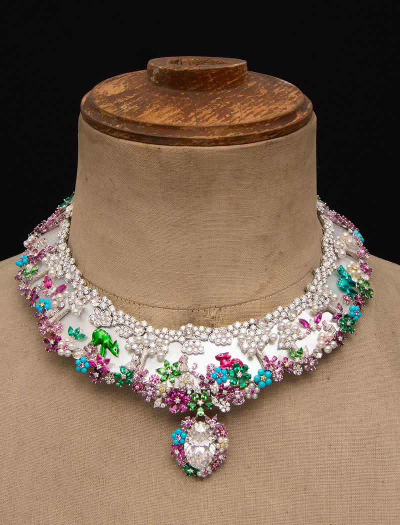 Necklace on a mannequin bust featuring white, green, pink, and turquoise gemstones and pearl beads, set against a dark background.