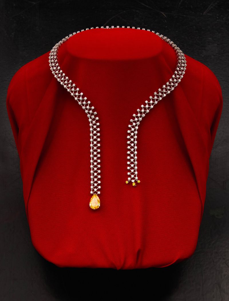Diamond collar necklace with a pear-cut yellow gemstone pendant displayed on a red bust against a dark backdrop.