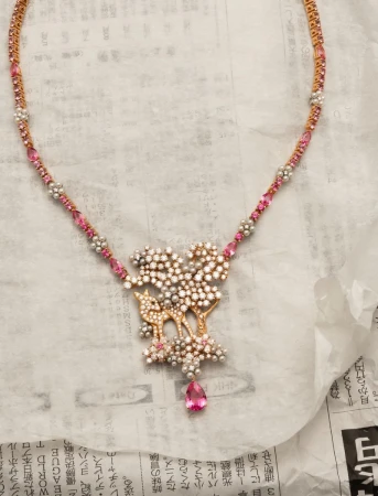 Dior High Jewelry necklace featuring a gold deer motif, diamond clusters, and pink gemstones on paper.