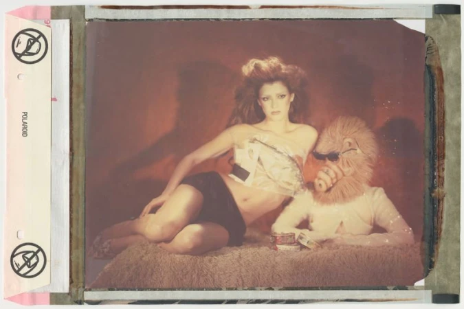 Polaroid portrait of an adult female reclining next to a person in a furry lion mask, capturing a surreal and artistic scene indoors.
