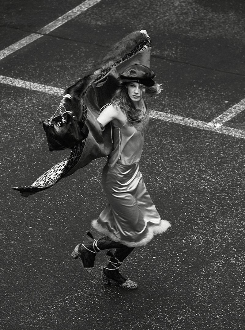 Overhead shot of a model in a slip dress, hat, and boots, striking a pose with a patterned wrap in an urban environment.