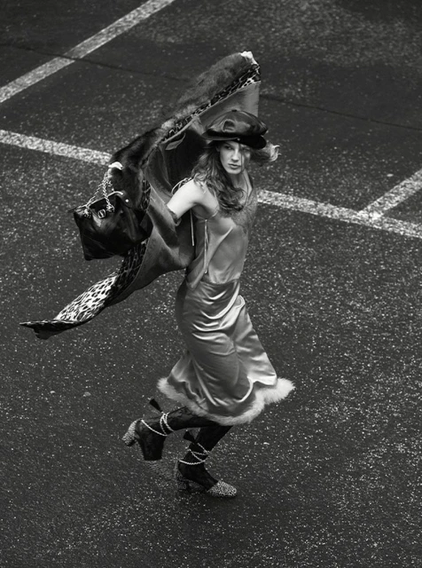 Overhead shot of a model in a slip dress, hat, and boots, striking a pose with a patterned wrap in an urban environment.