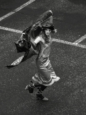 Overhead shot of a model in a slip dress, hat, and boots, striking a pose with a patterned wrap in an urban environment.