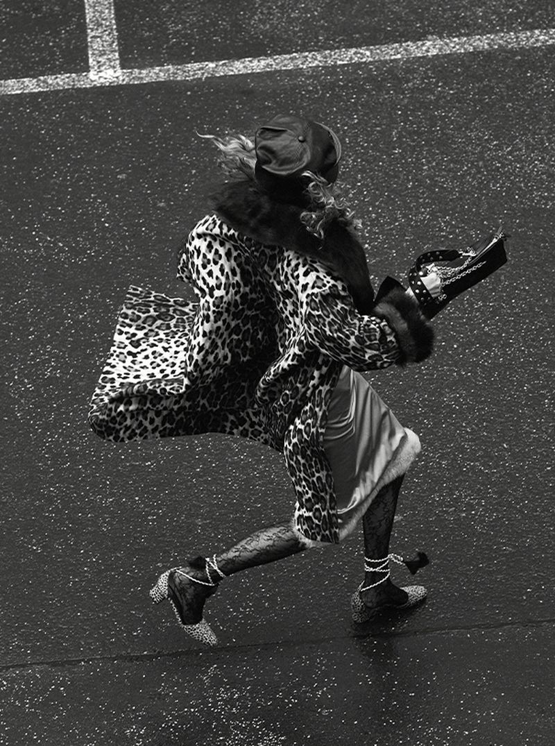 High-angle shot of a woman with an animal print coat and matching heels walking in an outdoor urban environment in black and white.