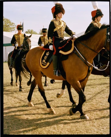 Four members of the Household Cavalry ride horses wearing ceremonial uniforms with black coats, gold trim, and red plumed hats.