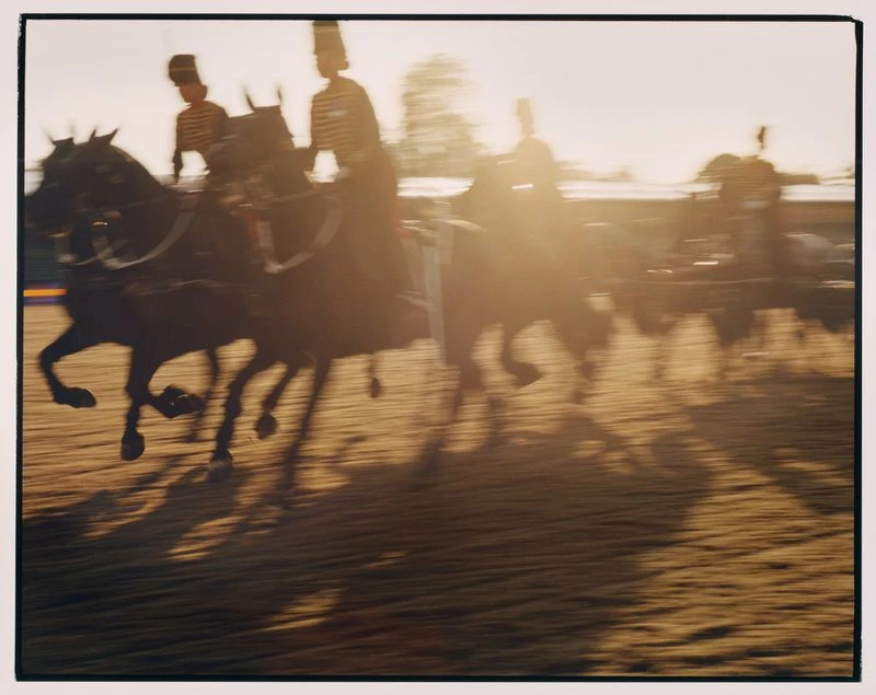 Men in uniform riding horses in motion, outdoor equestrian event, warm sunlight, shallow focus, artistic blur.