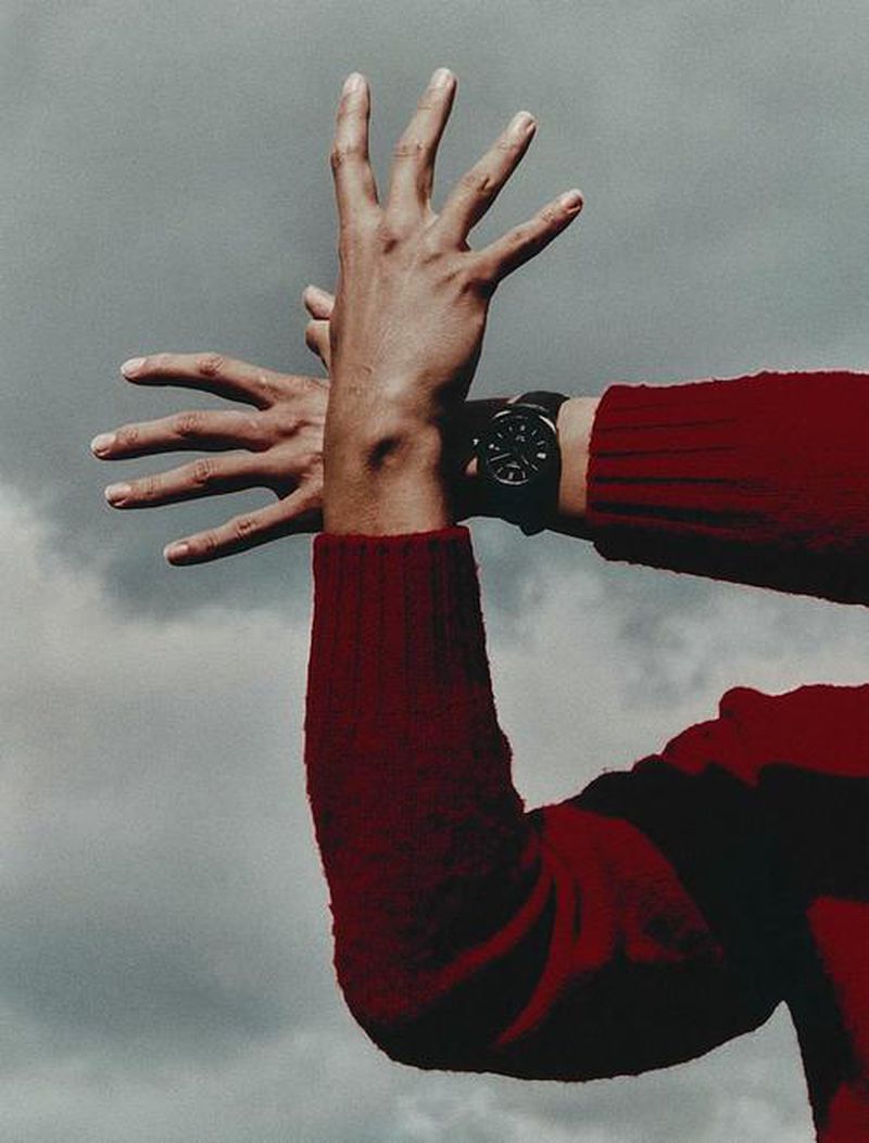 Two hands with extended fingers cast a shadow puppet against a cloudy sky, wrist with black watch visible, wearing a long-sleeved red shirt.