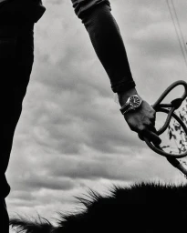 Black and white shot of a person wearing a metal wristwatch while holding a leash over a dog against an overcast sky.