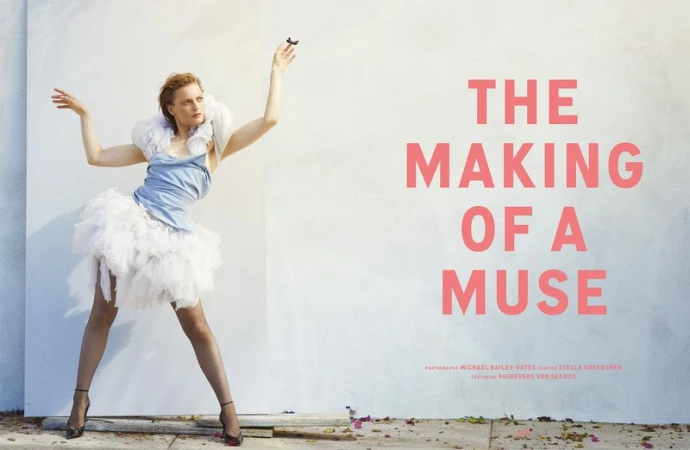 Model Guinevere van Seenus poses in a blue corset top and white tulle skirt against an outdoor wall backdrop with pink typography.