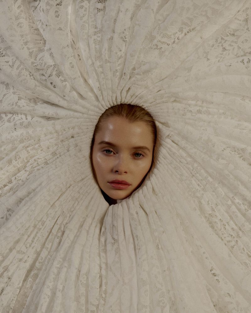 Striking close-up portrait of a model with light skin encircled by a white lace garment, creating a dramatic, ethereal aesthetic.