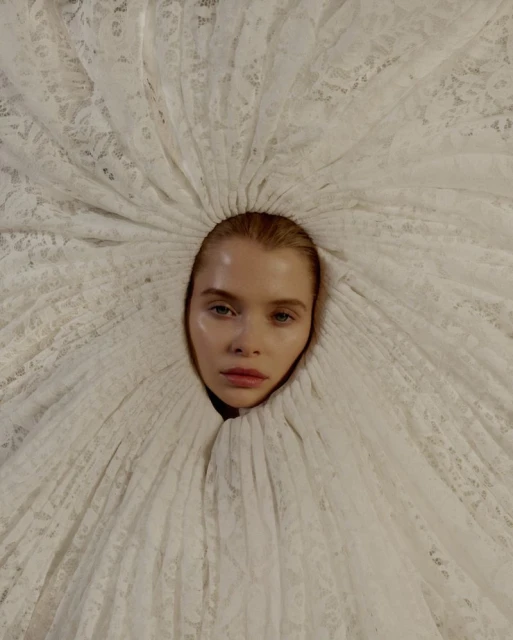 Striking close-up portrait of a model with light skin encircled by a white lace garment, creating a dramatic, ethereal aesthetic.