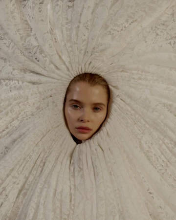 Striking close-up portrait of a model with light skin encircled by a white lace garment, creating a dramatic, ethereal aesthetic.