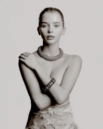 Woman posing with crossed arms wearing a chunky ribbed collar necklace, patterned cuff bracelet, and feather skirt on a studio backdrop.