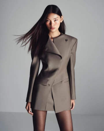 Fashion portrait of an Asian woman in a structured taupe blazer dress with black tights on a neutral grey background in a photo studio.
