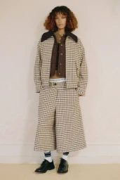 Model wearing a beige checkered jacket and matching wide-leg culottes with black dress shoes against a neutral backdrop.