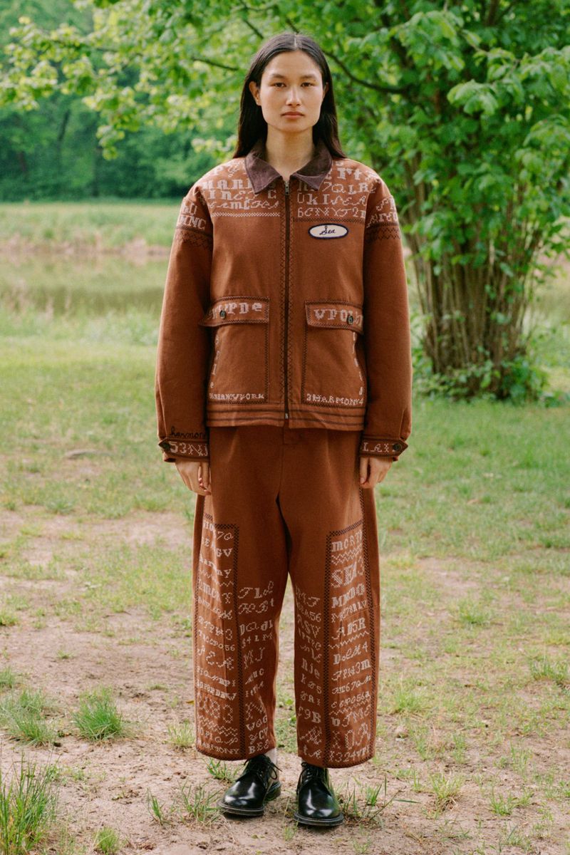 Asian woman in a brown embroidered jacket and pants standing outdoors. The fashion shot features a full-length view, showcasing nature.