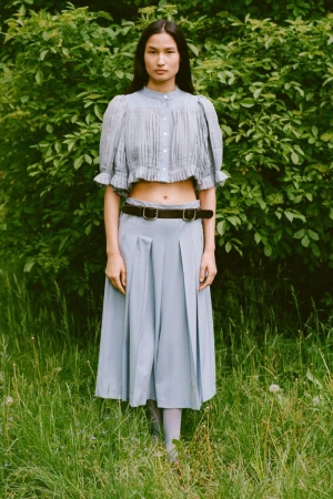 Model Varsha Thapa wearing a light blue pleated crop top and pleated midi skirt outdoors for Sea RS26 Lookbook.
