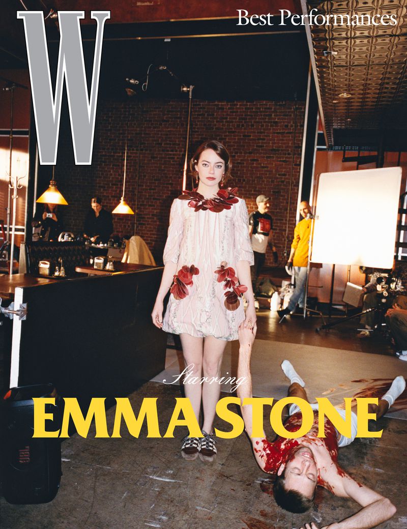 Emma Stone stars in a W Magazine cover. A second human is lying on the floor. Photo studio setting with a brick wall backdrop.