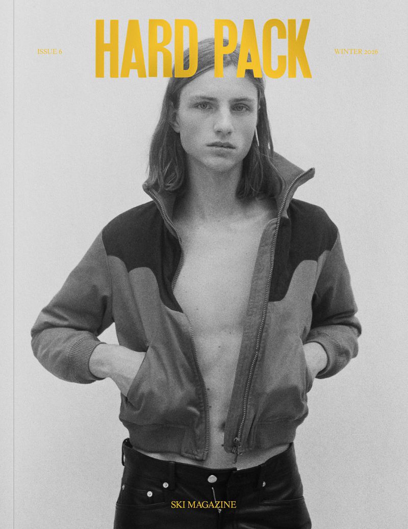 Magazine cover featuring an androgynous person with long hair, wearing a jacket and leather pants against a light background.