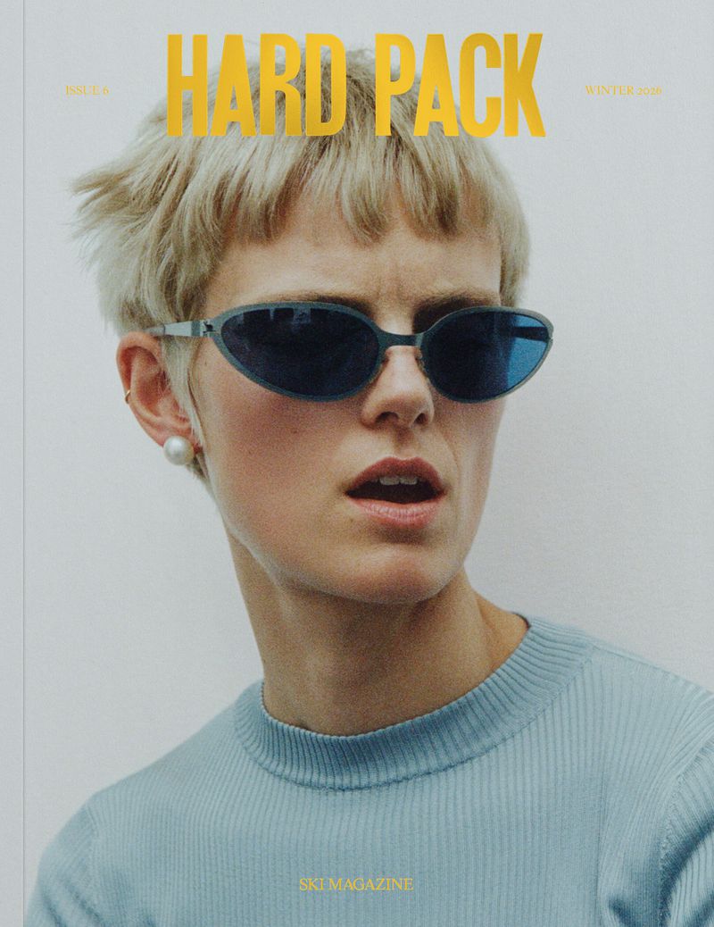 Blonde adult woman in sunglasses wearing a blue sweater poses for a magazine cover against a neutral-toned background.