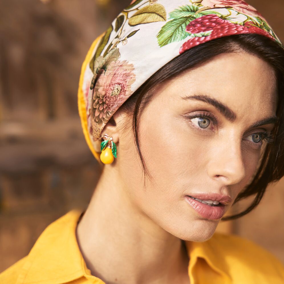 Close-up of a woman with floral headscarf and lemon earrings in an eye-level portrait, showcasing fashion and beauty elements.