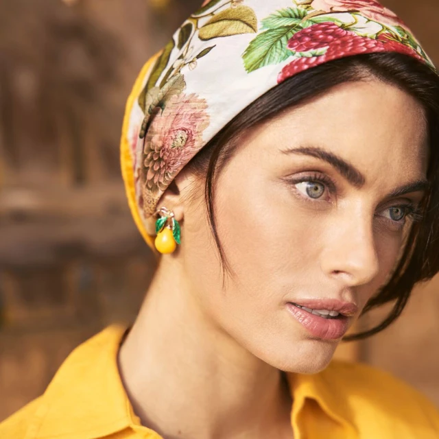 Close-up of a woman with floral headscarf and lemon earrings in an eye-level portrait, showcasing fashion and beauty elements.