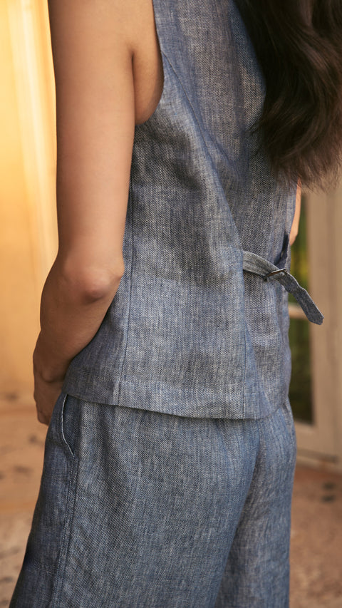 Woman wearing blue linen vest and pants. Sleeveless top with back belt detail. Casual fashion concept.