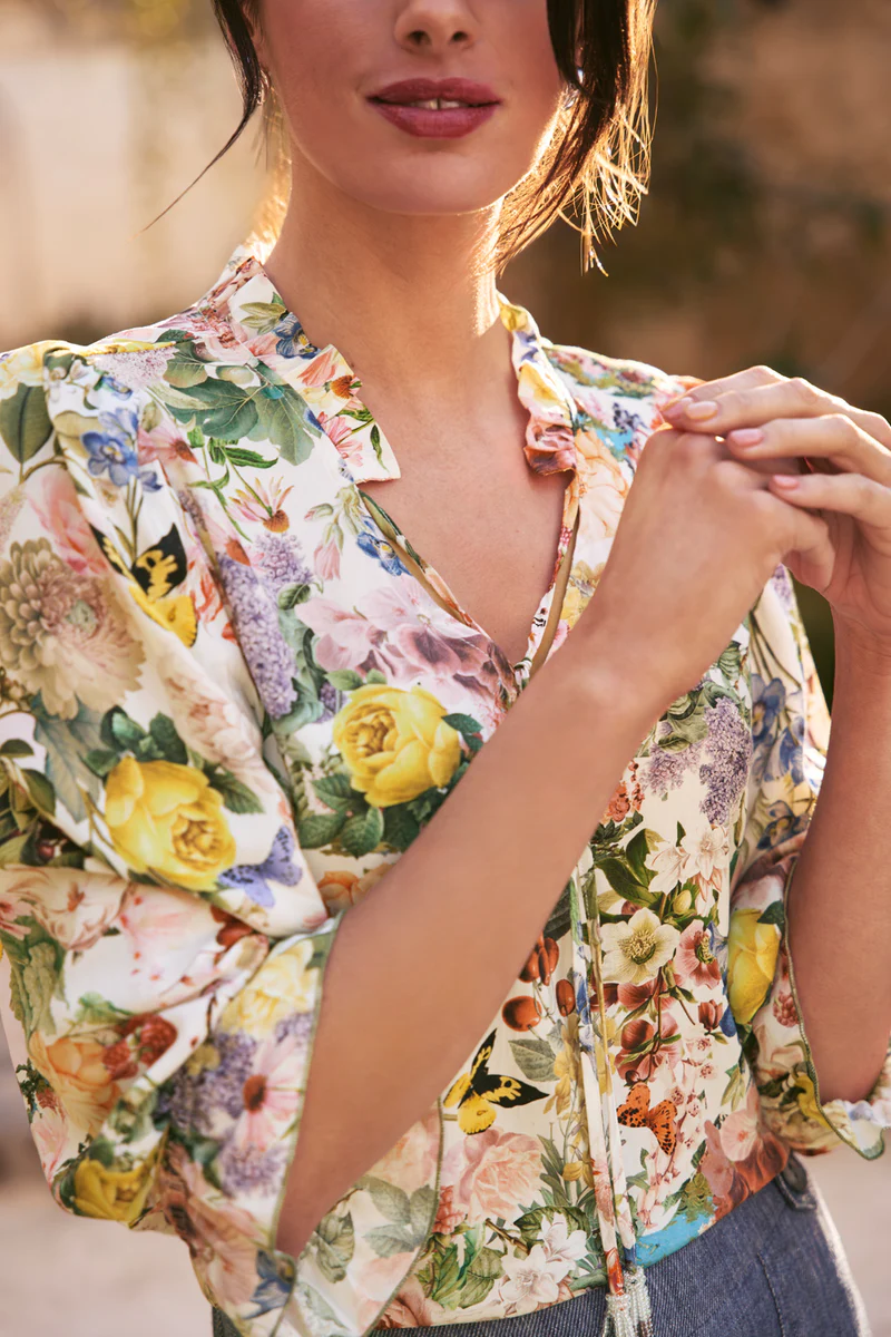 Close-up of an adult woman wearing a floral-patterned blouse with a ruffle collar in soft, diffused, natural light.