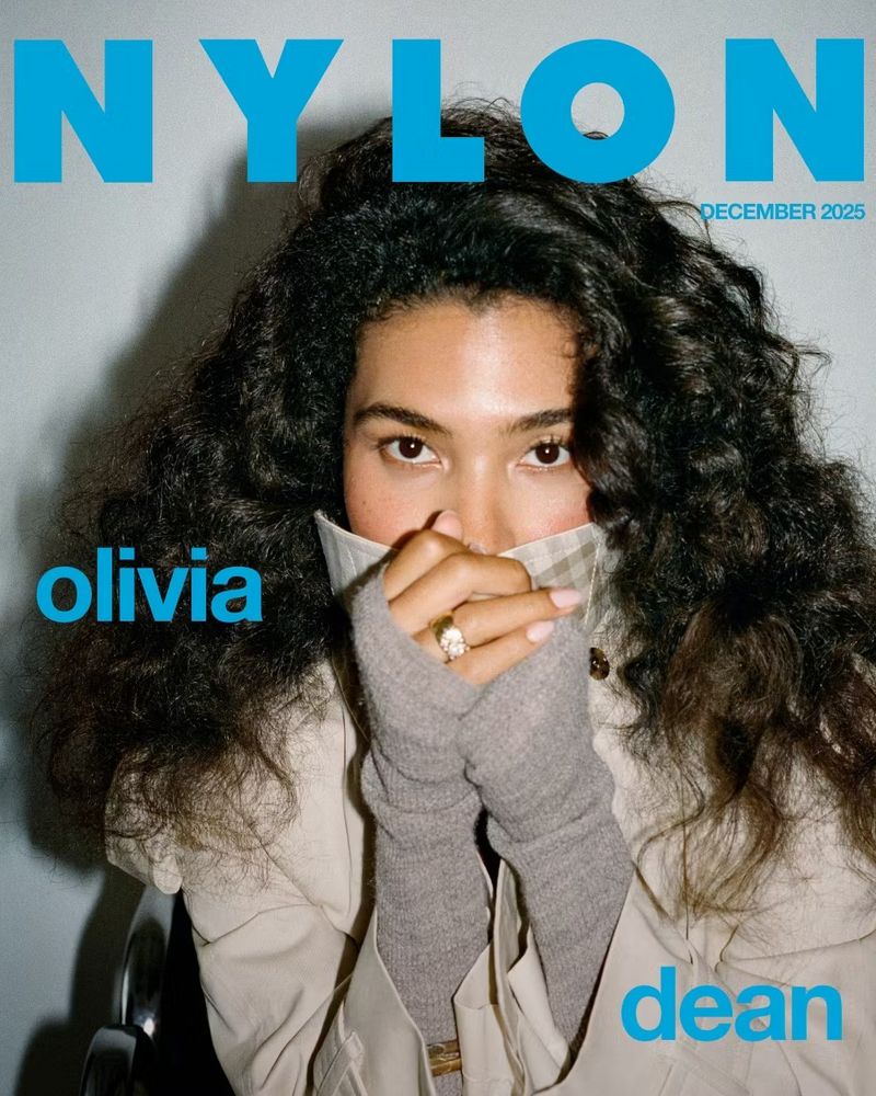 Magazine cover featuring a young woman with curly hair wearing a tan trench coat and grey gloves, posing with hands to her face.