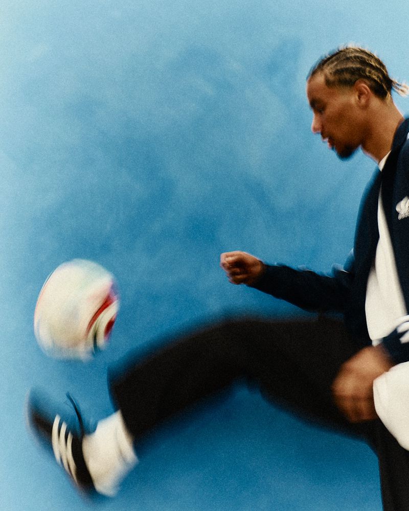 Adult male in sportswear kicks soccer ball against a blue wall indoors, showcasing fitness and sports activity with blurred motion.