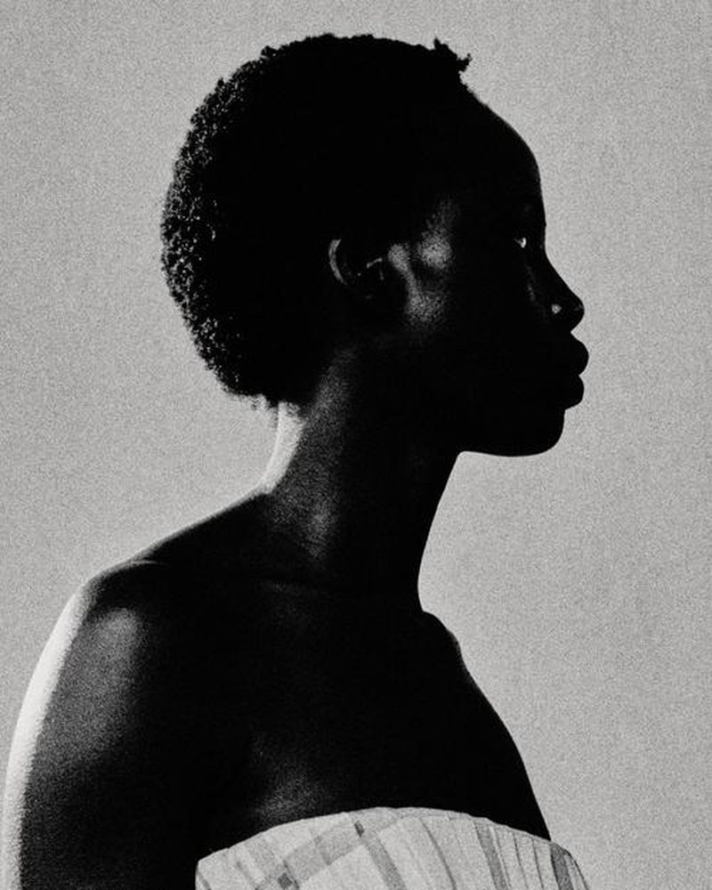 Striking profile portrait of an adult African woman with a short curly hairstyle, wearing a striped top against a neutral background.