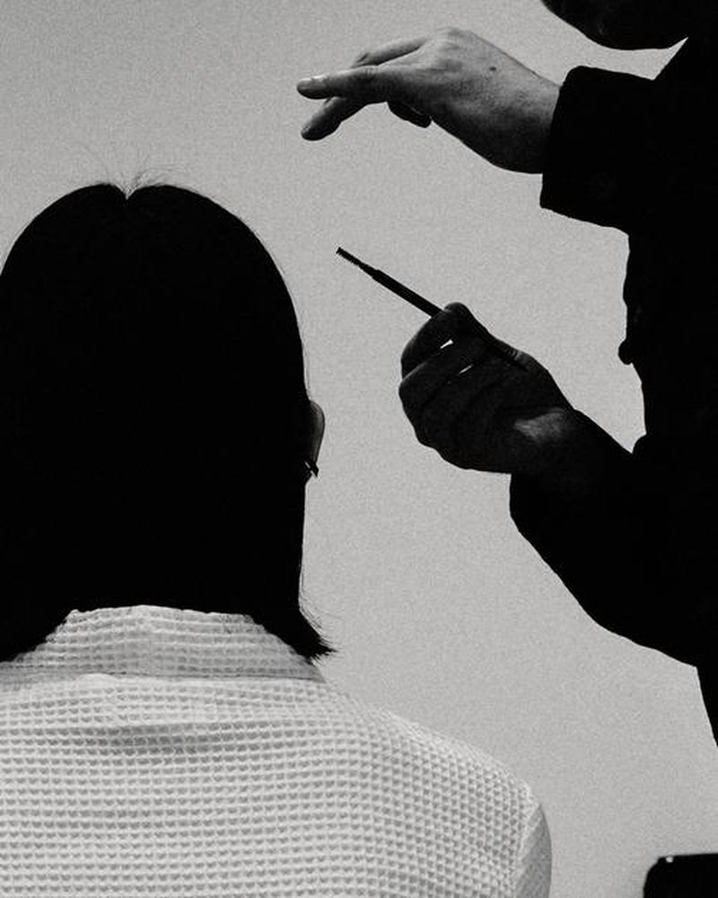 Adult woman getting makeup applied by a makeup artist in a monochromatic photo studio, showcasing beauty and fashion industries.