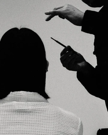 Adult woman getting makeup applied by a makeup artist in a monochromatic photo studio, showcasing beauty and fashion industries.
