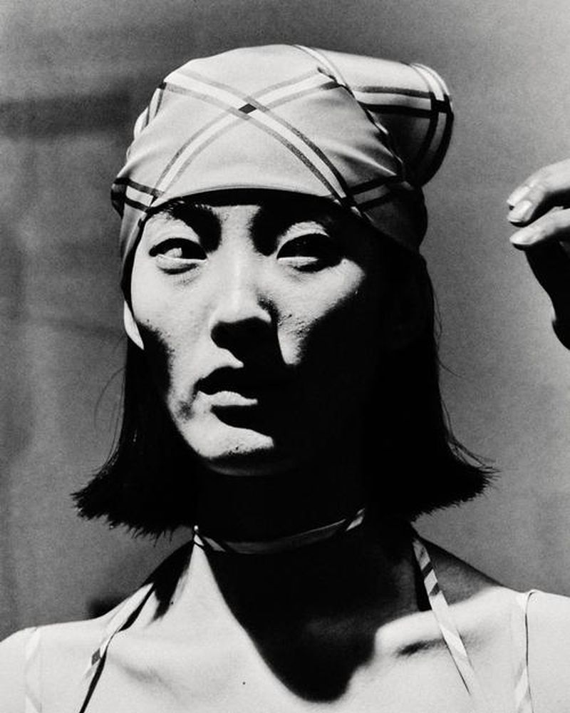Striking black and white portrait of an adult female with a patterned headscarf and choker, set against a simple background.