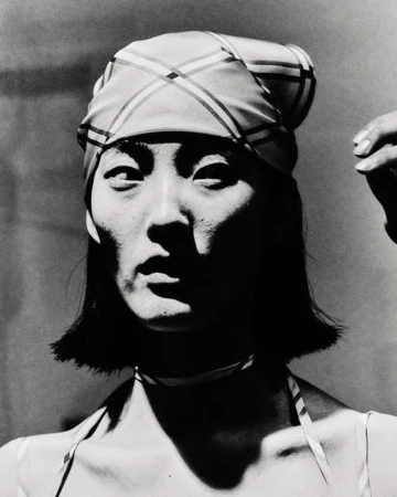 Striking black and white portrait of an adult female with a patterned headscarf and choker, set against a simple background.
