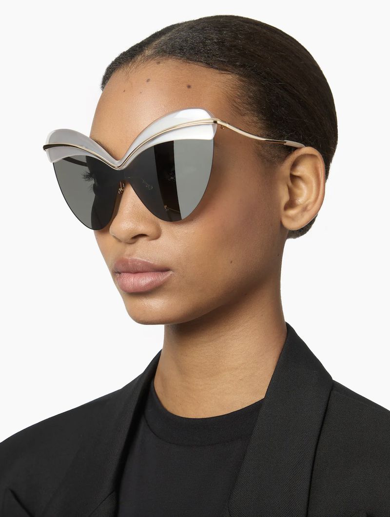 Elegant studio shot of a woman wearing oversized butterfly sunglasses with silver and gold frames against a clean, bright white background.