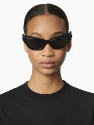 Model wearing black cat-eye sunglasses and a black crewneck top against a white background