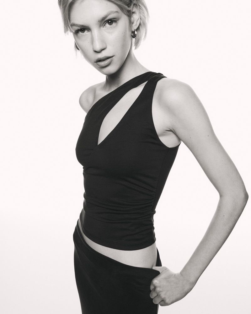 Monochrome portrait of a woman in a black, cutout top and skirt. She poses in a studio with a neutral expression and neutral background.