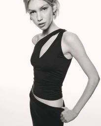 Model in a black asymmetrical top and dark skirt against a plain white seamless studio background.