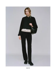 Model wearing a black jacket and trousers holding a woven handbag against a grey backdrop