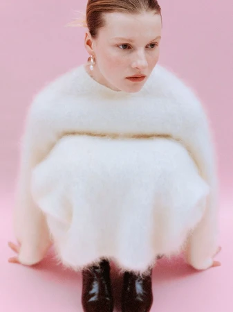 Fashion shot featuring a model in a fluffy white sweater and dark patent leather shoes, posing against a pastel pink backdrop.