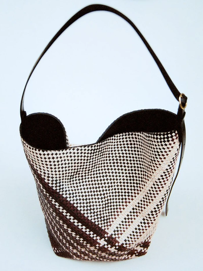 Woven bucket handbag with dark leather strap against a clean white background