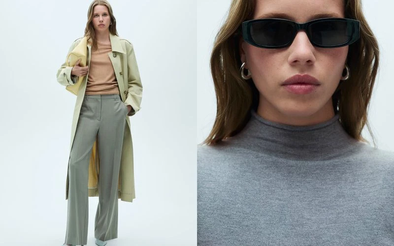 Two women in an indoor fashion setting. One wears a trench coat and grey trousers. The other wears sunglasses and a grey turtleneck.