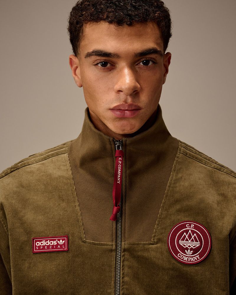 Close-up of a young adult man in a corduroy Adidas x C.P. Company jacket, looking at the camera against a neutral background.