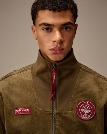 Close-up of a young adult man in a corduroy Adidas x C.P. Company jacket, looking at the camera against a neutral background.