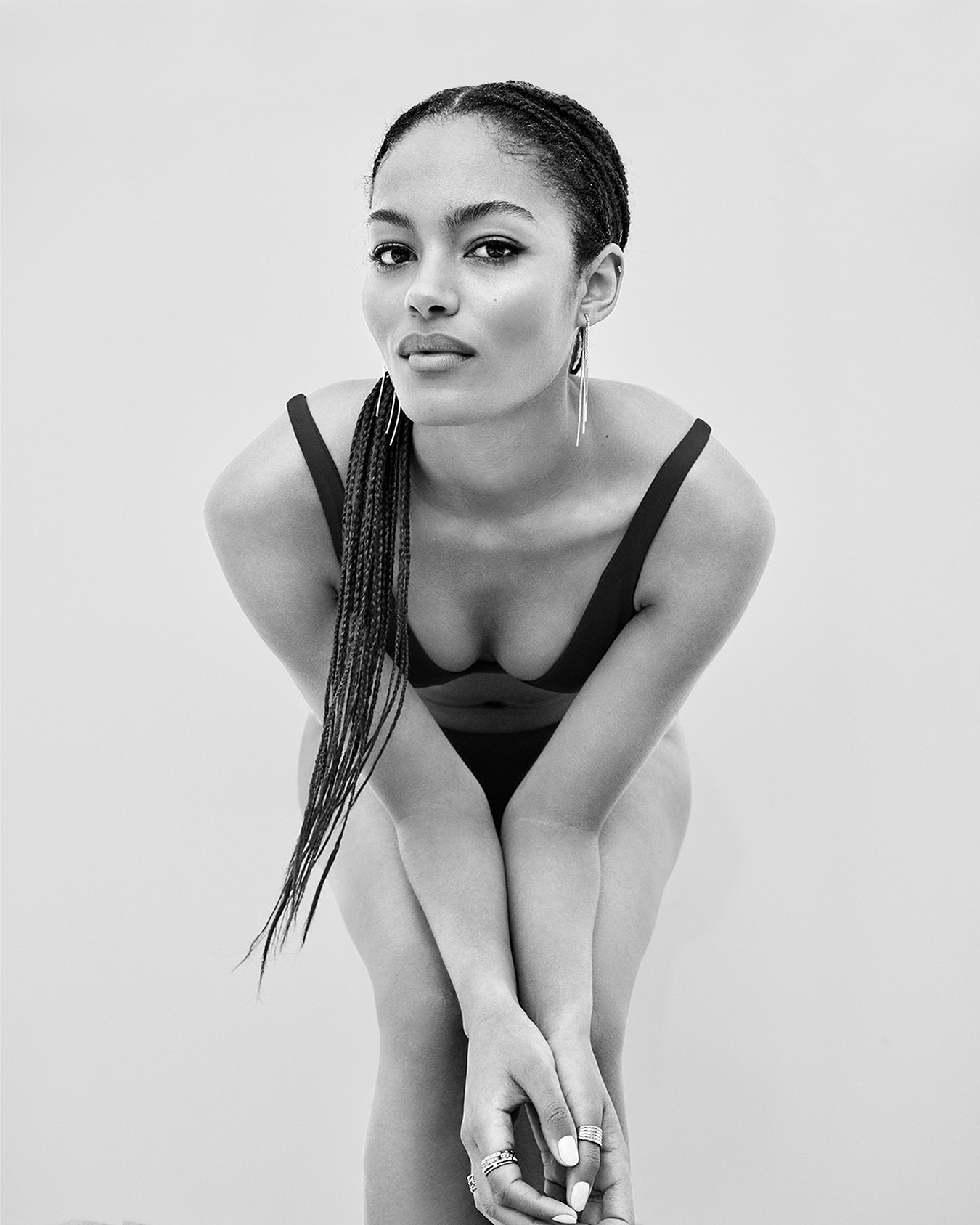 Monochromatic portrait of an adult woman with braided hair posing in a studio with hands clasped, gazing directly at the camera.